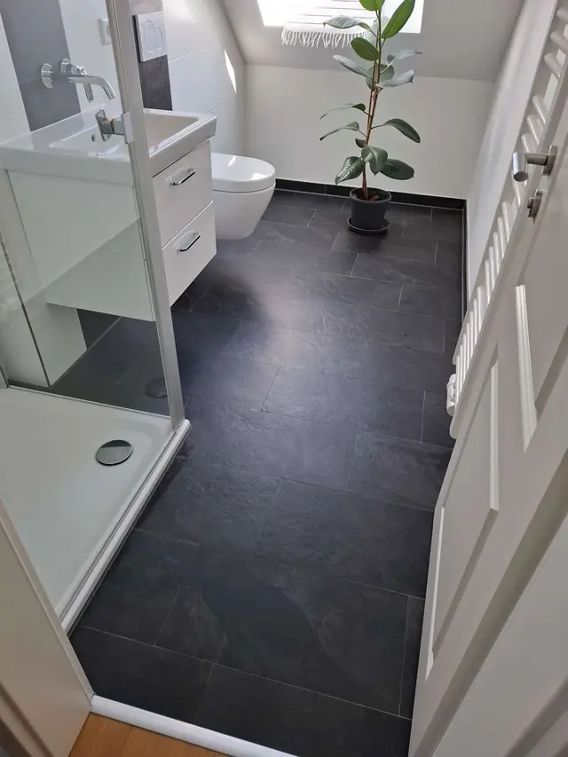 Gereinigtes Badezimmer mit dunklem Schieferboden, Waschtisch und Pflanze
